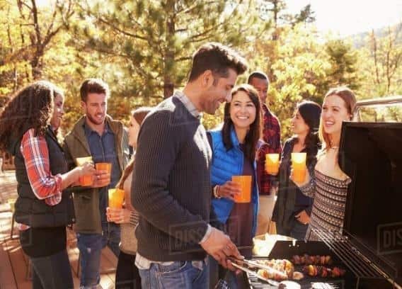 Group of friends stand at a barbecue, one cooking at grill - Stock Photo - Dissolve